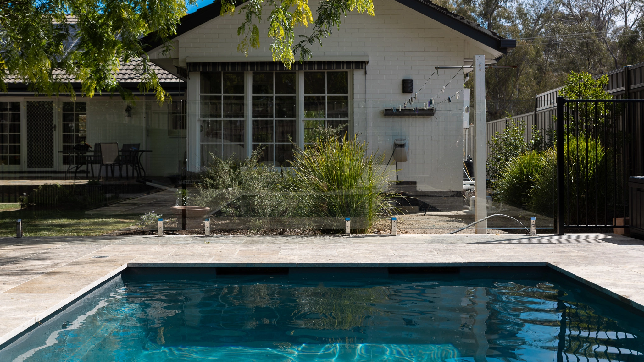 The Precision 6.00m fibreglass swimming pool is installed in front of a white countryside farmhouse, with greenery and mountains surrounding it. The mysterious Graphite Grey gives a modern look to the overall countryside aesthetics.