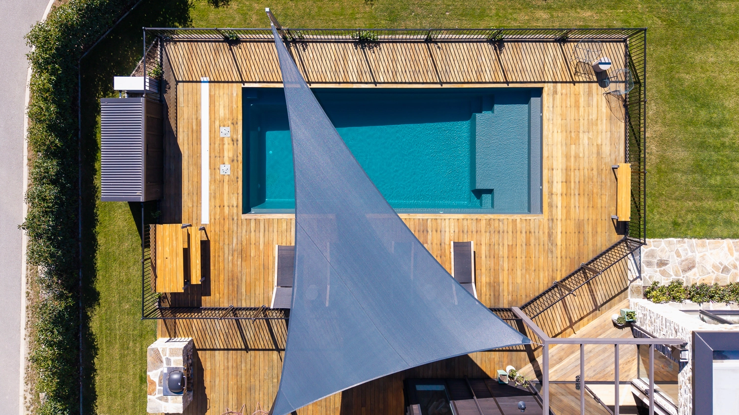 The Acclaim 10.20m fibreglass swimming pool is installed in a mountainous region of Central Otago, New Zealand. The house is surrounded by wooden tiles and natural greenery with mountains in the background. The pool colour is Graphite Grey, which stands out from the resort-like landscape and wooden house.
