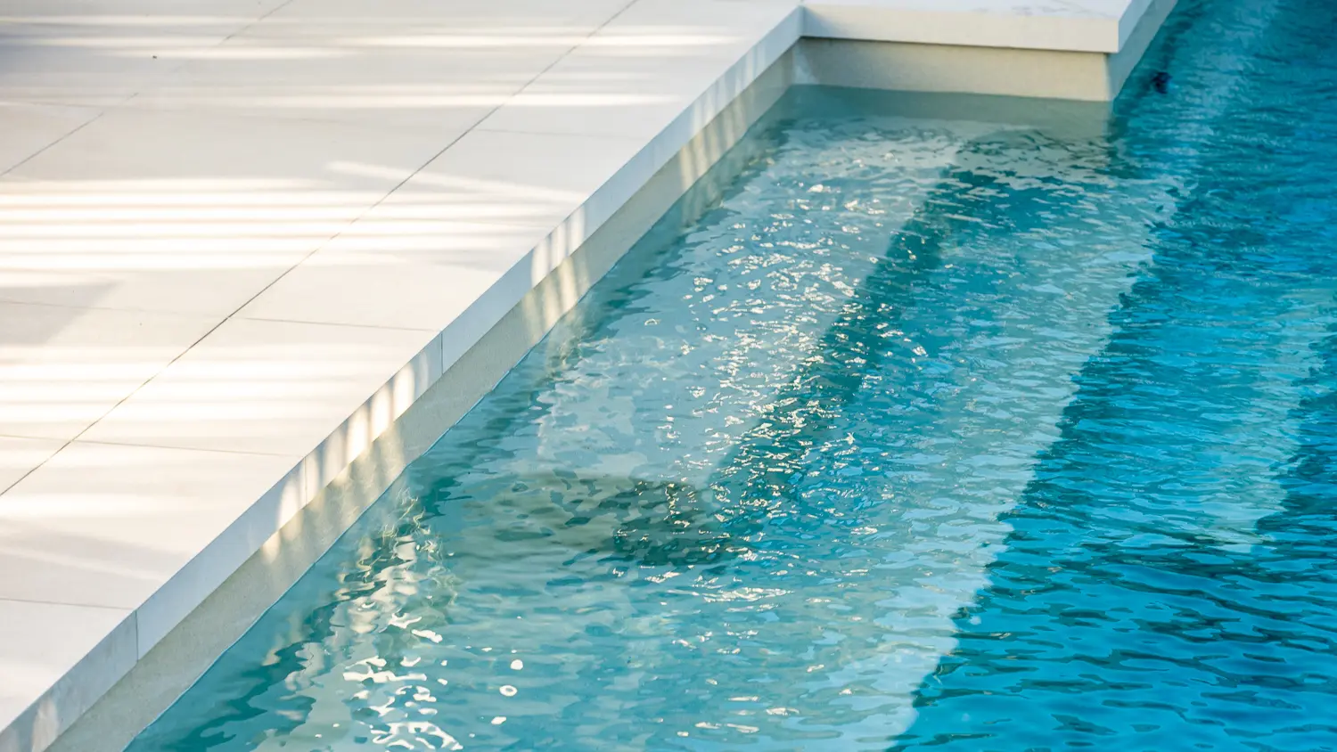 The Elegance 10.00m fibreglass swimming pool is installed in a metropolitan region of Central Otago, New Zealand. The house is surrounded by wooden tiles and natural greenery with mountains in the background. The pool colour is Diamond Sand, which stands out from the resort-like landscape and wooden house.